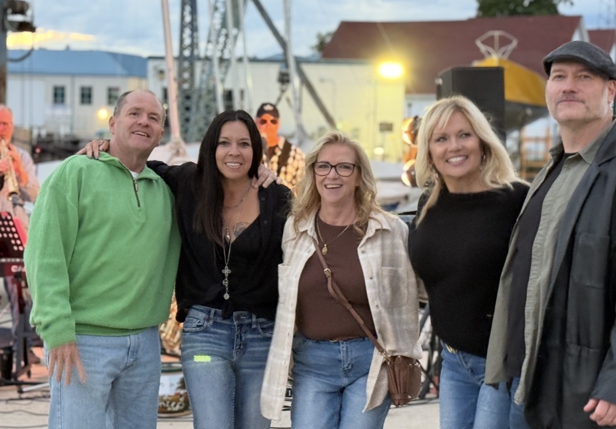 Five attendees smiling together in front of live music